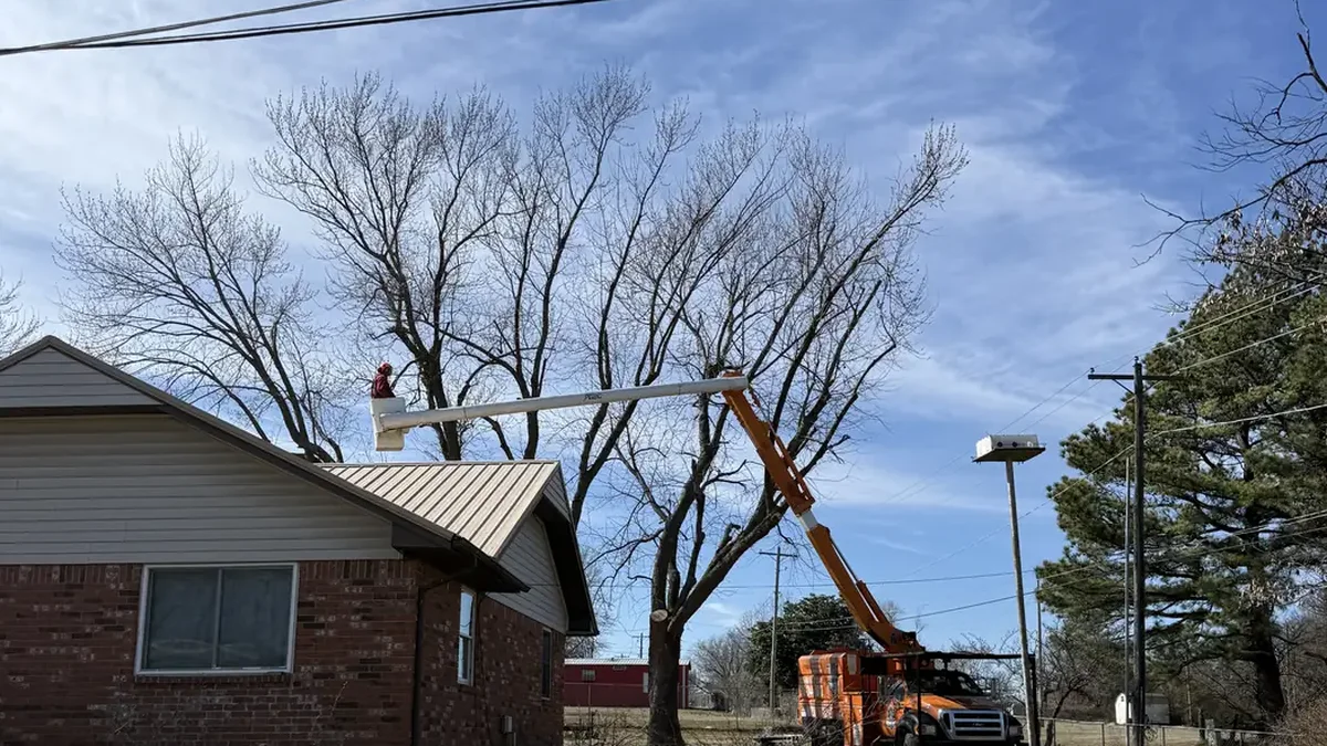 Ironwood Tree Service bucket truck removing a tree near a house roofline in Tulsa, OK