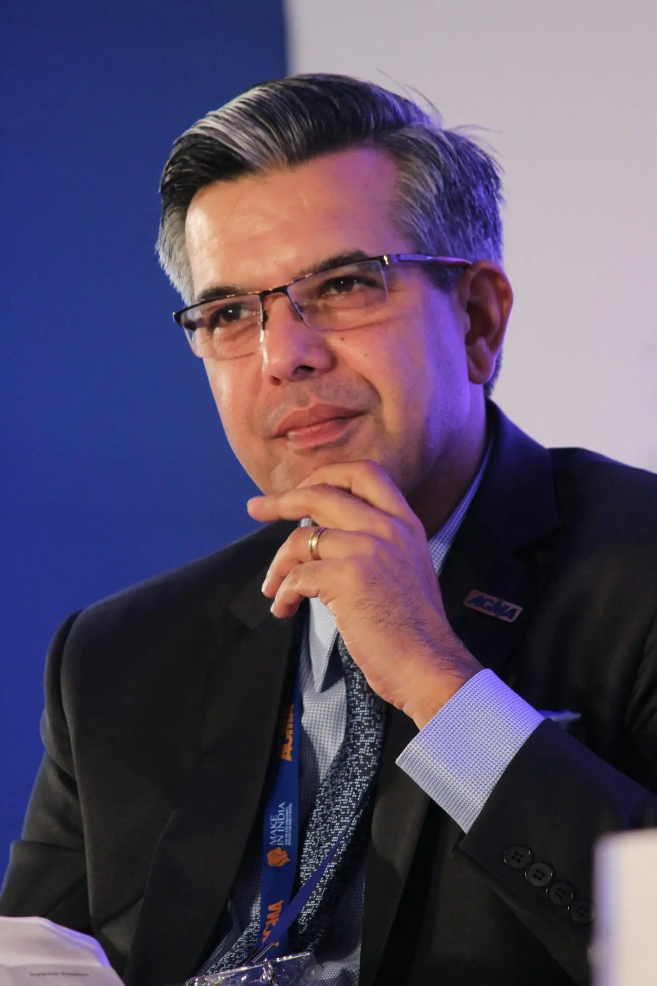 Testimonials Portrait of a thoughtful businessman in a suit, wearing eyeglasses, captured in an indoor corporate setting.